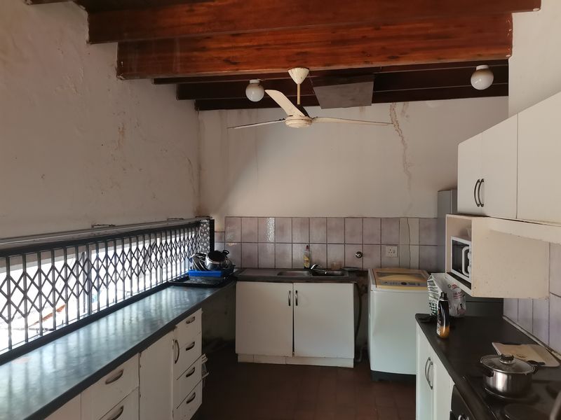 A functional kitchen featuring exposed timber ceiling beams, tiled splashback, and built-in cabinetry, requiring cosmetic updates to address wall cracks and general wear.