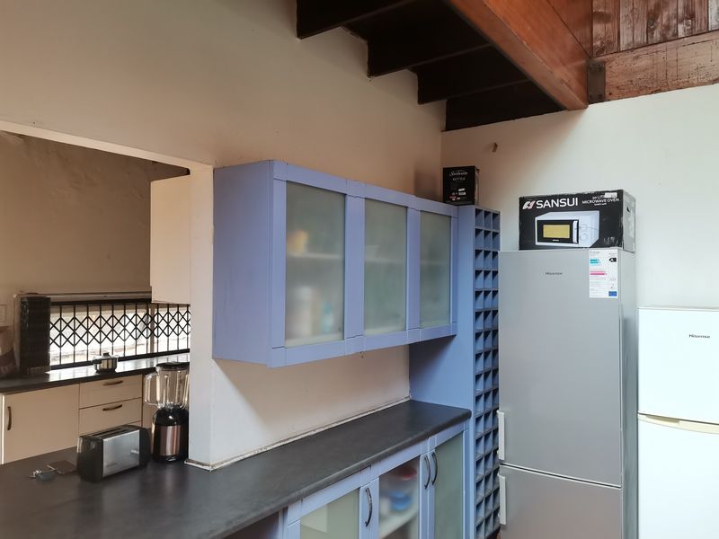 Kitchen area featuring blue built-in cabinetry, dark countertops, a wine rack, and exposed timber ceiling beams, offering a functional layout with potential for updates.