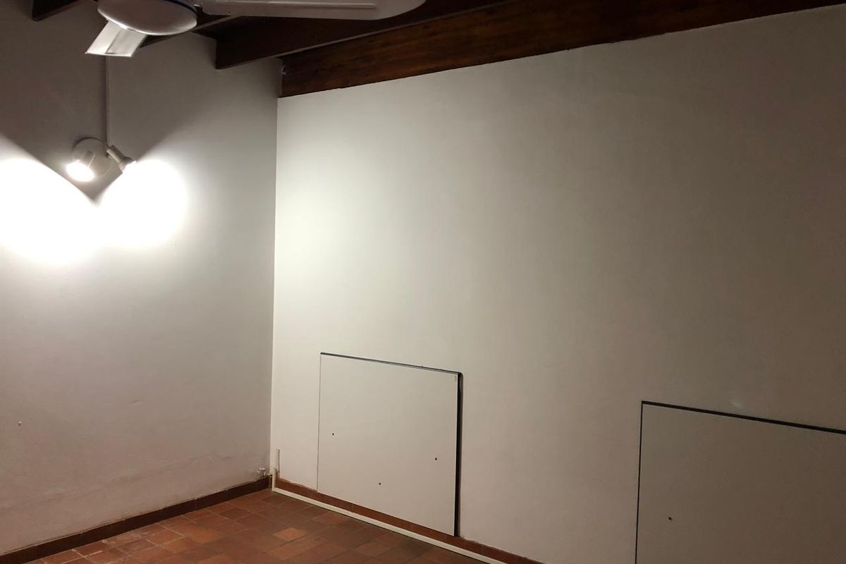 An empty bedroom featuring exposed timber ceiling beams, terracotta floor tiles, and built-in wall access panels.