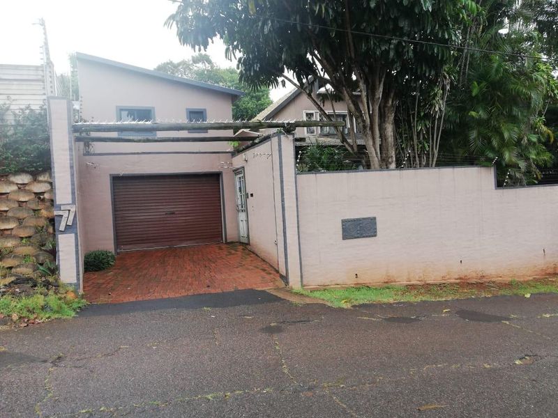 Front exterior view of the property featuring a roller garage door, brick paved driveway, and secure perimeter wall with electric fencing.