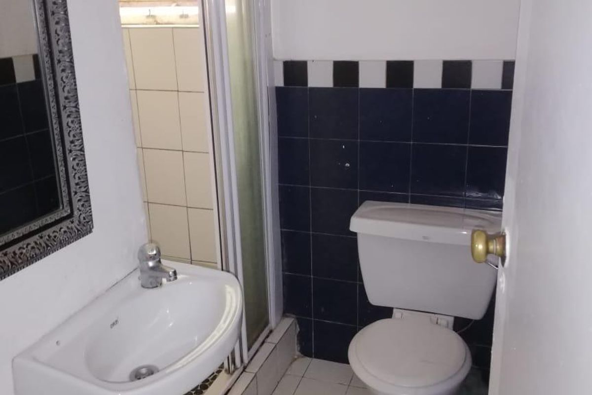 A compact bathroom featuring a pedestal basin, a shower enclosure, and a toilet with dated black and white tiled accents.