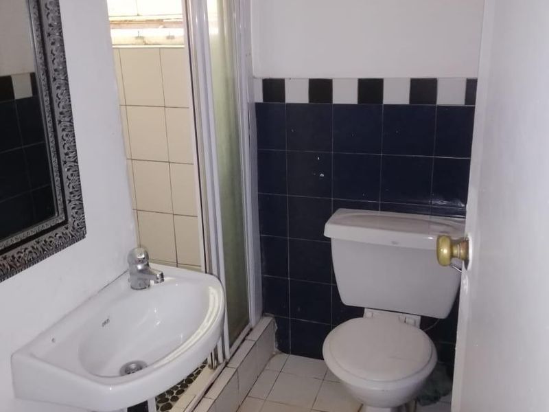 A compact bathroom featuring a pedestal basin, a shower enclosure, and a toilet with dated black and white tiled accents.