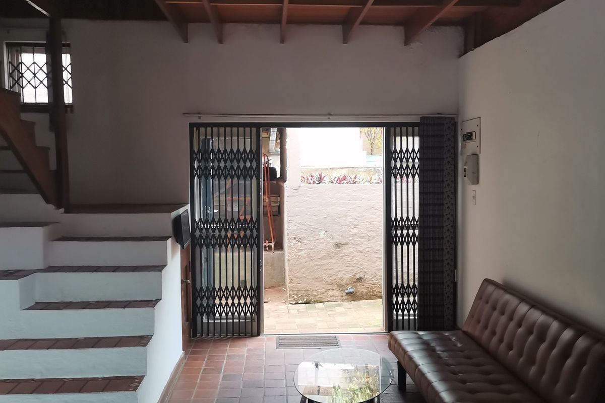 Living room featuring exposed timber beam ceilings, terracotta tile flooring, and a staircase, with direct access to an outdoor area through a security gate.