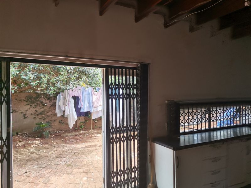 A covered patio area featuring exposed timber beams, built-in cabinetry, and a security gate leading to a paved outdoor space.