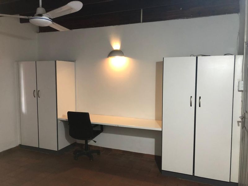 A functional home office featuring built-in cupboards, a wall-mounted desk, ceiling fan, and tiled flooring.