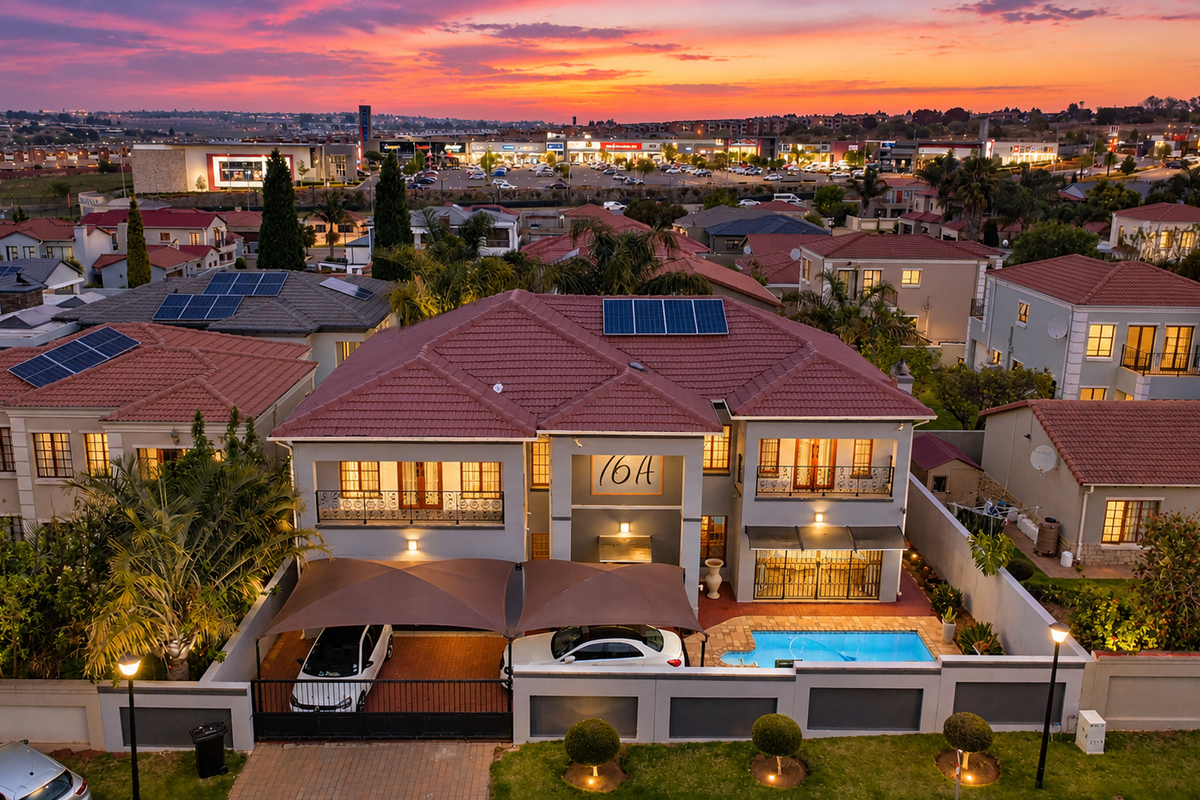 Aerial view of a residential property featuring a tiled roof with solar panels, a swimming pool, and a covered carport area at sunset.