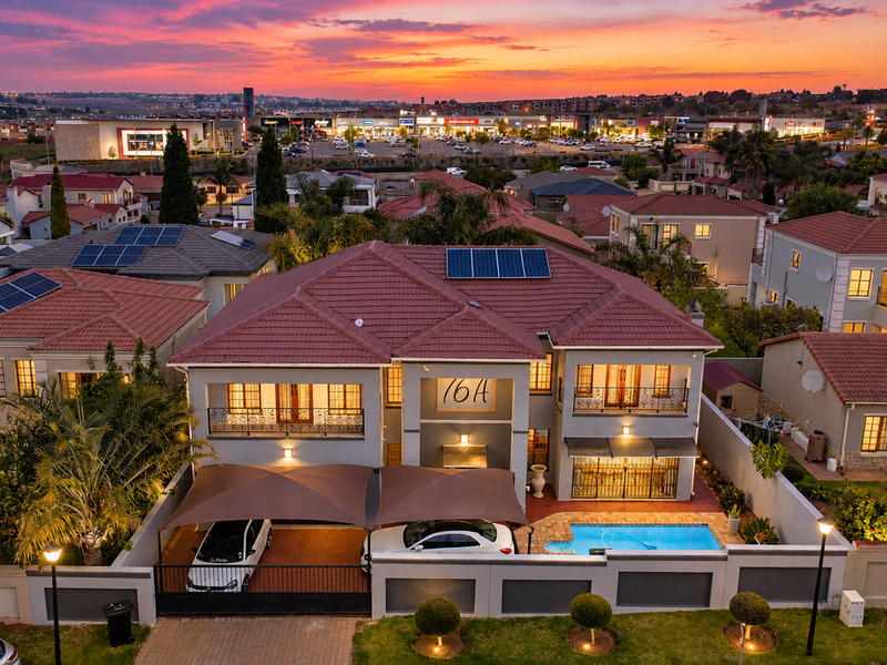 Aerial view of a residential property featuring a tiled roof with solar panels, a swimming pool, and a covered carport area at sunset.