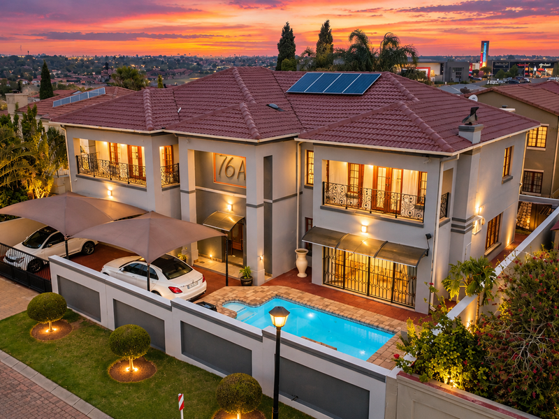 Stunning double-story residence featuring a tiled roof with solar panels, a private swimming pool, secure carport, and well-maintained landscaped garden at sunset.