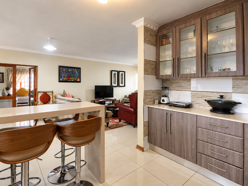 Open plan kitchen and living area featuring modern wood-finish cabinetry, stone countertops, tiled backsplash, and a breakfast bar with tiled flooring throughout.