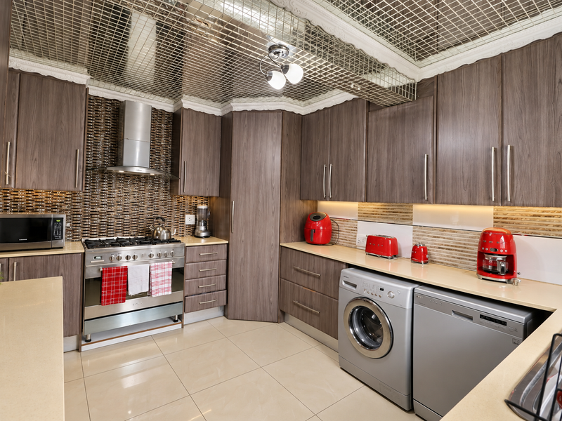 Modern kitchen featuring wood-grain cabinetry, stone countertops, stainless steel appliances, mosaic backsplash, and a unique mirrored grid ceiling design.