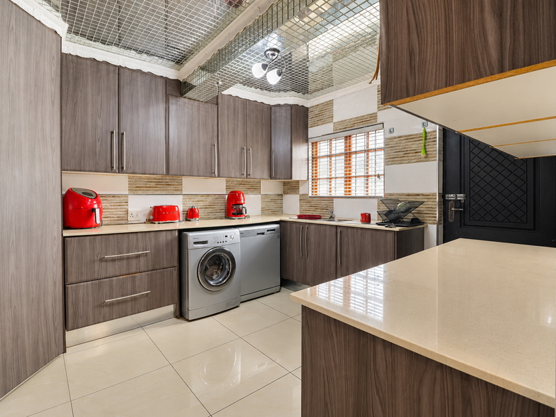 Modern kitchen featuring wood-grain cabinetry, stone countertops, integrated appliances, and a unique mirrored ceiling finish with tiled flooring.