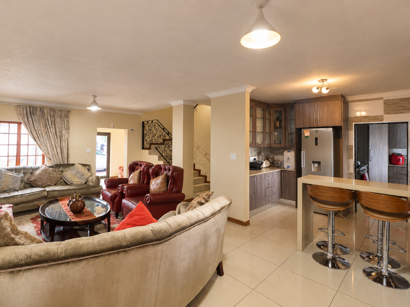 Open-plan living and kitchen area featuring tiled floors, modern cabinetry, a breakfast bar, and a staircase with decorative wrought iron railing.