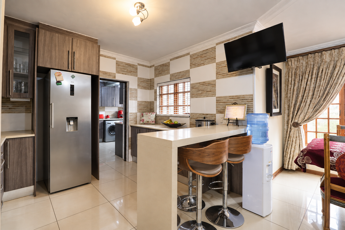 A functional kitchen featuring wood-finish cabinetry, a stone breakfast bar, and tiled wall accents, with an adjacent scullery area visible.