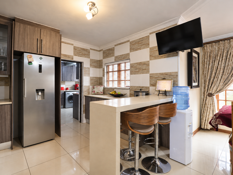 A functional kitchen featuring wood-finish cabinetry, a stone breakfast bar, and tiled wall accents, with an adjacent scullery area visible.