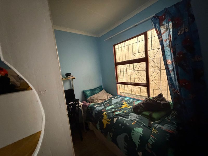 A compact bedroom featuring a window with security bars and blue painted walls, requiring minor cosmetic updates to improve the overall finish.