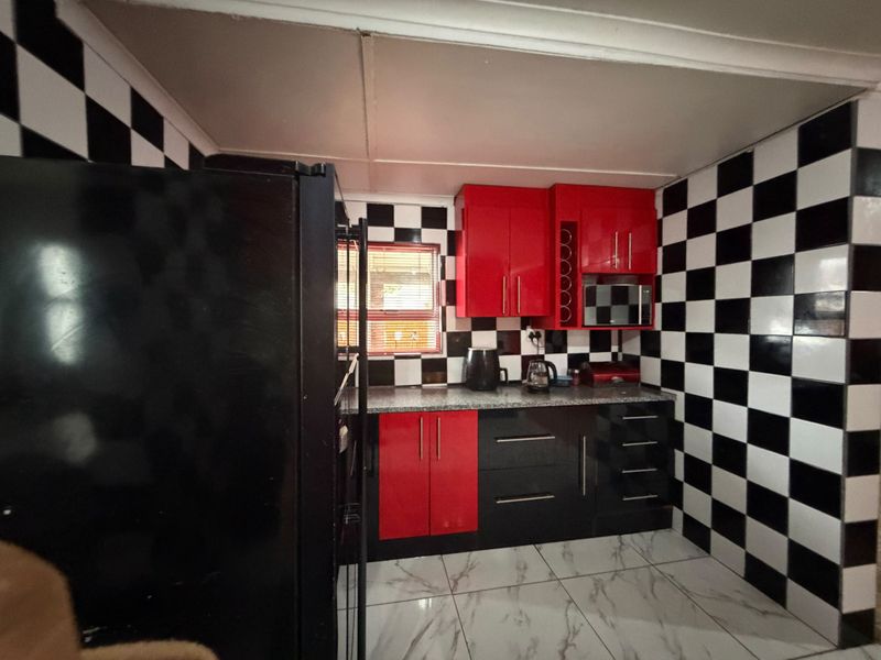 A compact kitchen featuring high-contrast black and white checkered wall tiles, red and black cabinetry, granite countertops, and modern floor tiles.