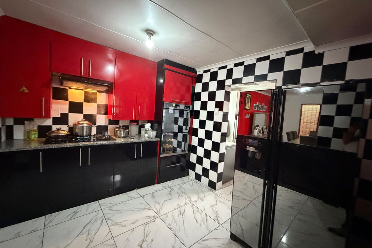 A kitchen featuring high-gloss red and black cabinetry, a checkerboard backsplash, granite countertops, and modern marble-look floor tiles.