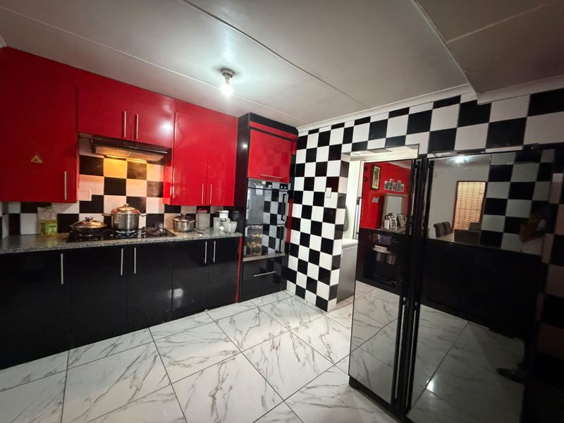 A kitchen featuring high-gloss red and black cabinetry, a checkerboard backsplash, granite countertops, and modern marble-look floor tiles.