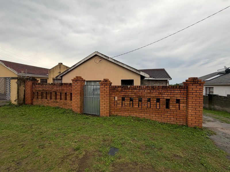 Front view of a single-story house featuring a brick boundary wall with a metal gate and a tiled roof.