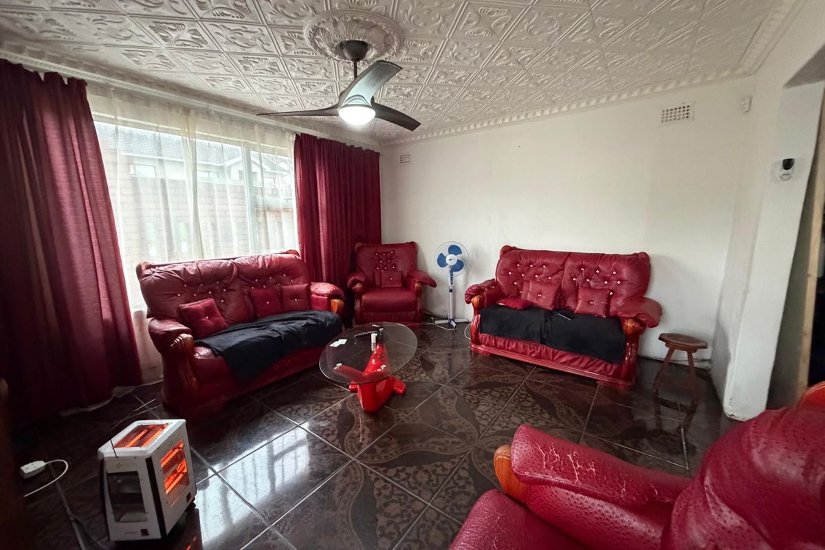 A living room featuring decorative ceiling tiles, a central ceiling fan, and dark patterned floor tiles.
