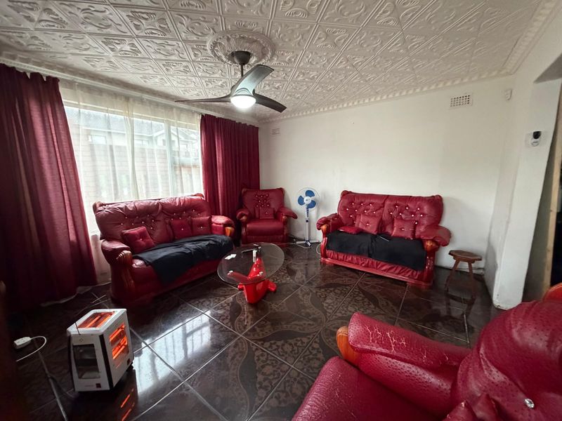 A living room featuring decorative ceiling tiles, a central ceiling fan, and dark patterned floor tiles.