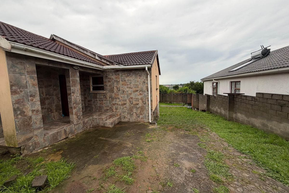Rear exterior view of the property featuring a tiled facade, covered patio area, and a concrete block boundary wall with a small garden space.