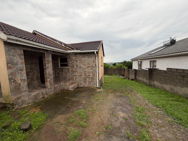 Rear exterior view of the property featuring a tiled facade, covered patio area, and a concrete block boundary wall with a small garden space.