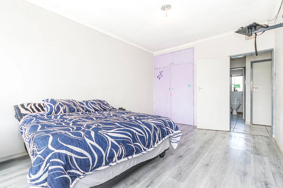 A bedroom featuring laminate flooring, built-in cupboards, and direct access to an adjoining bathroom.