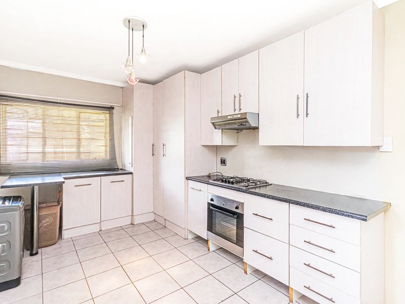 A functional kitchen featuring light-toned built-in cabinetry, a gas hob with extractor fan, built-in oven, and tiled flooring.