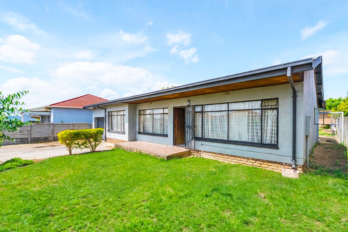 Rear view of the property featuring a brick patio, metal-framed windows, and a well-maintained lawn area.