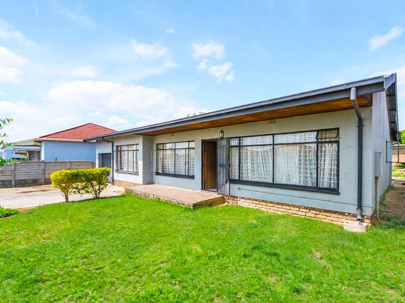 Rear view of the property featuring a brick patio, metal-framed windows, and a well-maintained lawn area.