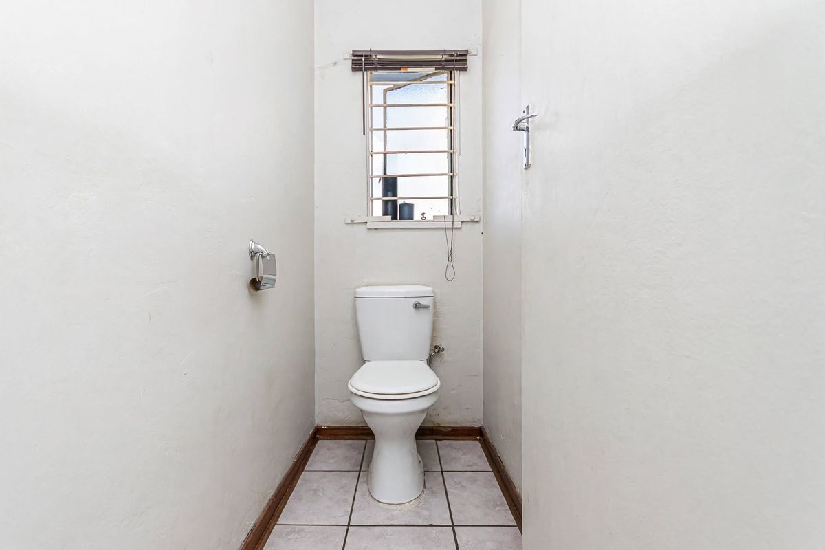 A compact, functional guest toilet featuring tiled flooring, a standard white toilet suite, and a window with security bars.