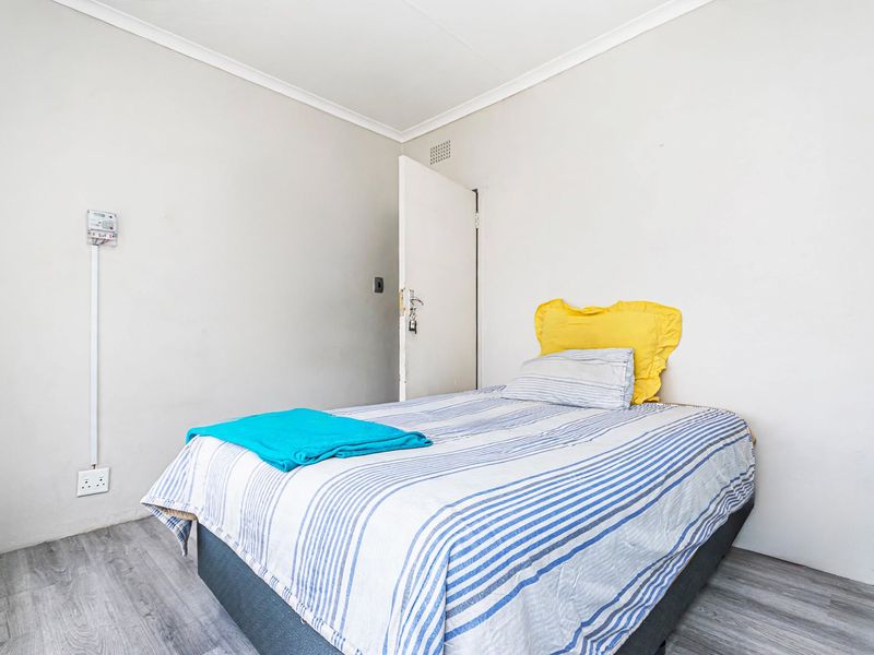 A simple bedroom featuring light-toned flooring, neutral walls, and a standard door, providing a functional and clean living space.