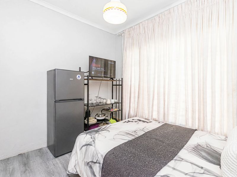 A functional bedroom featuring light-toned laminate flooring and large window curtains, providing a neutral base for personalization.