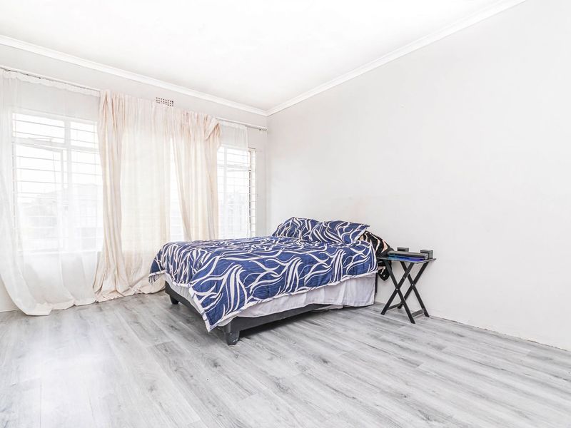A bedroom featuring light-toned laminate flooring, large windows with security bars, and neutral wall finishes.