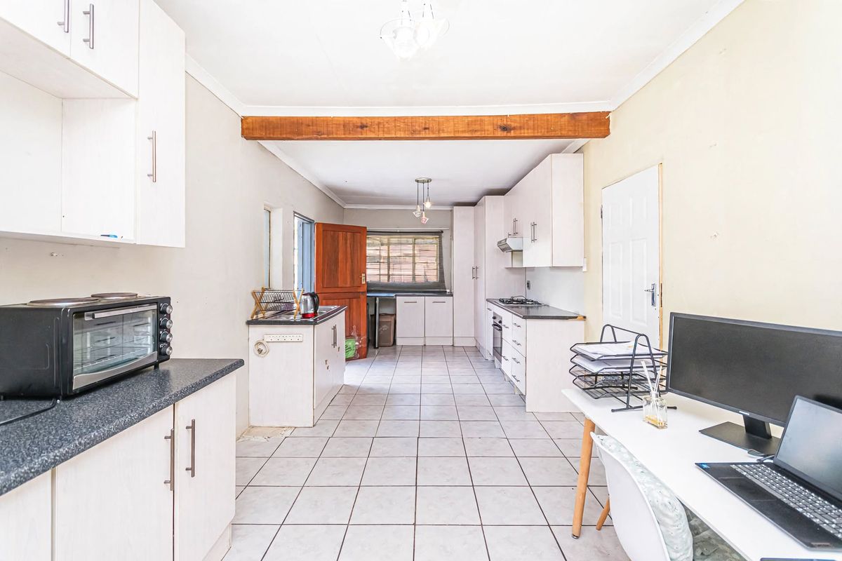 A functional kitchen featuring built-in cabinetry, laminate countertops, a built-in oven, hob, and extractor fan, finished with tiled flooring and an exposed timber beam.