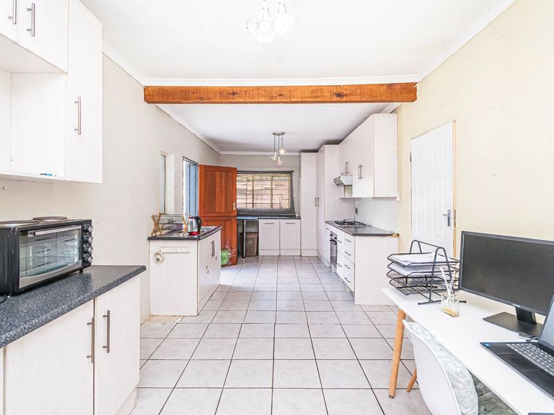 A functional kitchen featuring built-in cabinetry, laminate countertops, a built-in oven, hob, and extractor fan, finished with tiled flooring and an exposed timber beam.