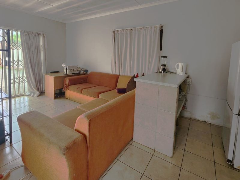 Open plan living area featuring tiled flooring, a breakfast counter, and access to an outdoor area through a security gate and sliding door.