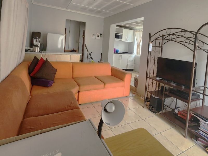 Open plan living area featuring tiled flooring and a connected kitchen space with built-in cabinetry and appliances.