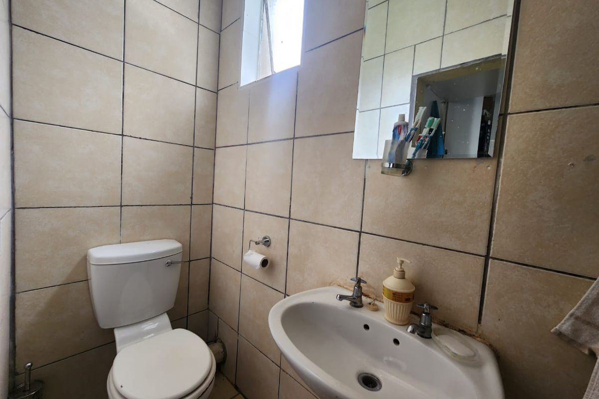 A compact bathroom featuring a pedestal basin, toilet, and fully tiled walls with a small window for natural light.