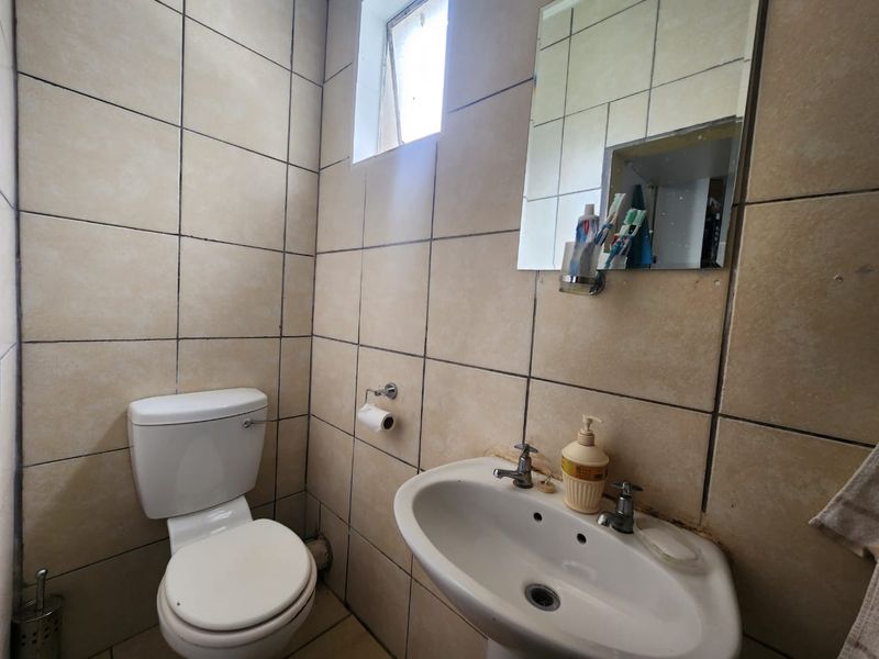 A compact bathroom featuring a pedestal basin, toilet, and fully tiled walls with a small window for natural light.