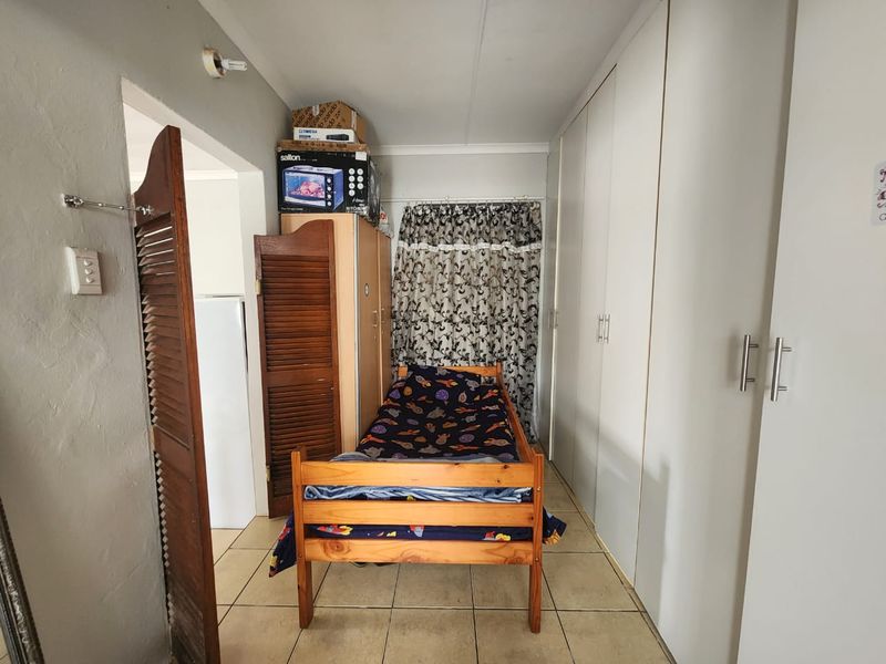 A compact bedroom featuring extensive built-in cupboard storage and tiled flooring, offering a functional space with potential for modern updates.