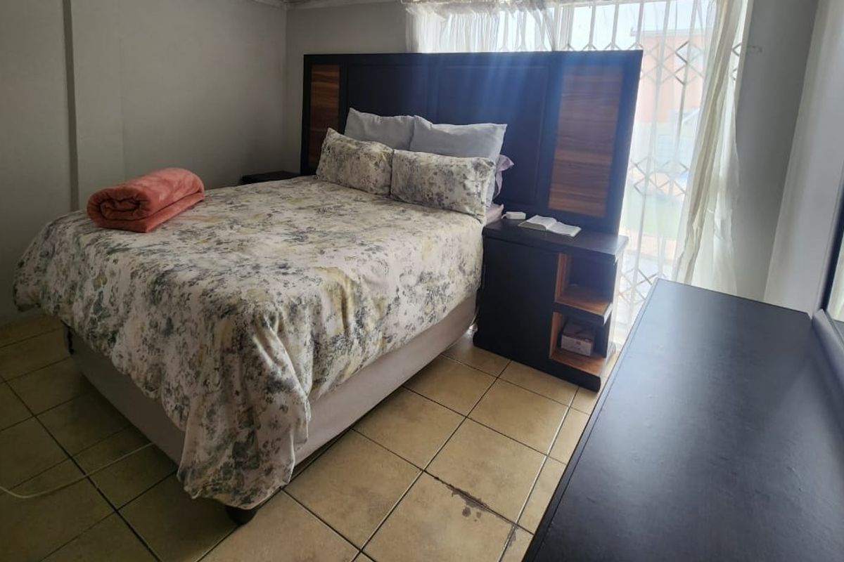 A bedroom featuring tiled flooring and a window with security bars, providing a functional space with standard finishes.