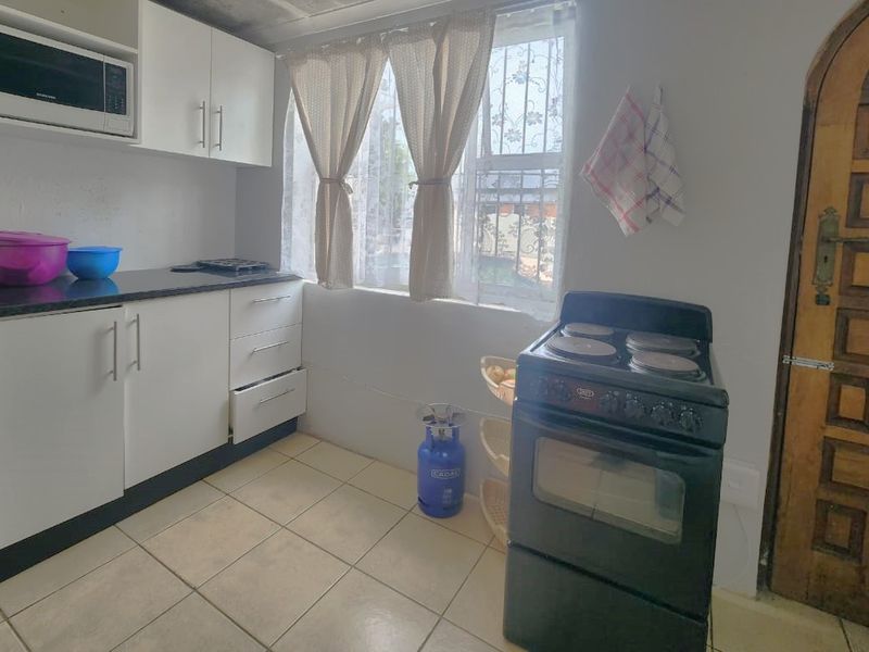 A functional kitchen featuring white built-in cabinetry, a dark laminate countertop, built-in microwave, and tiled flooring with security features on the window and door.