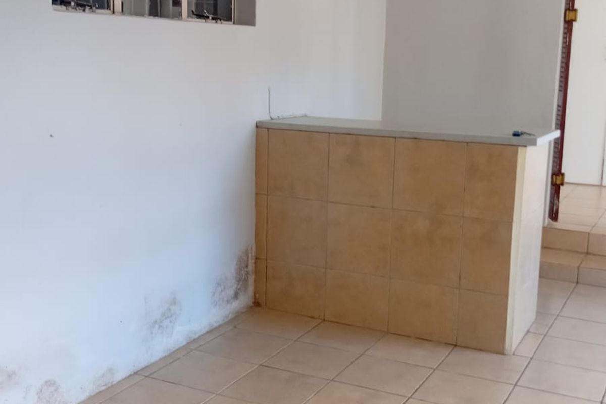An empty living area featuring tiled flooring and a built-in tiled counter, showing signs of wall dampness requiring maintenance.