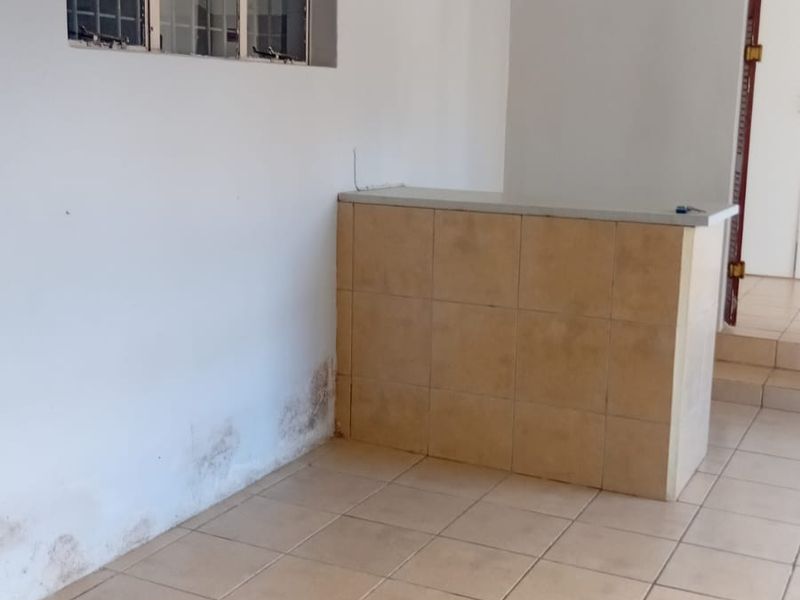 An empty living area featuring tiled flooring and a built-in tiled counter, showing signs of wall dampness requiring maintenance.