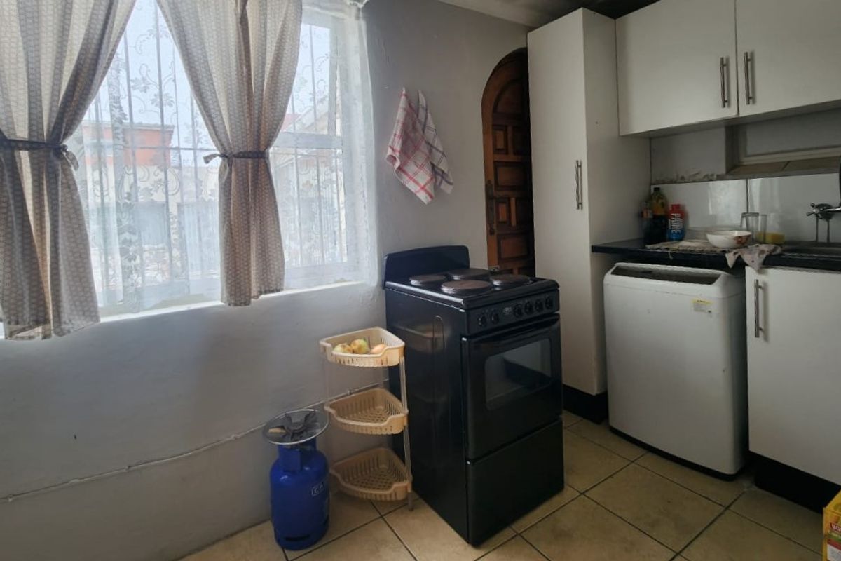 A compact kitchen featuring built-in cabinetry, a freestanding stove, and tiled flooring, offering a functional space with potential for modernization.