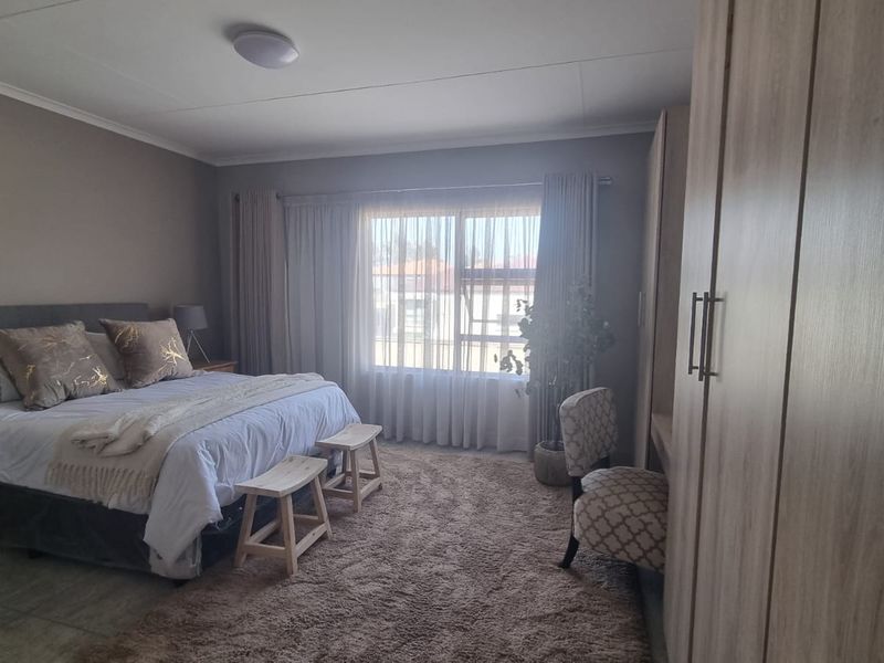 A well-maintained bedroom featuring neutral wall tones, large windows with natural light, and integrated built-in cupboards for storage.