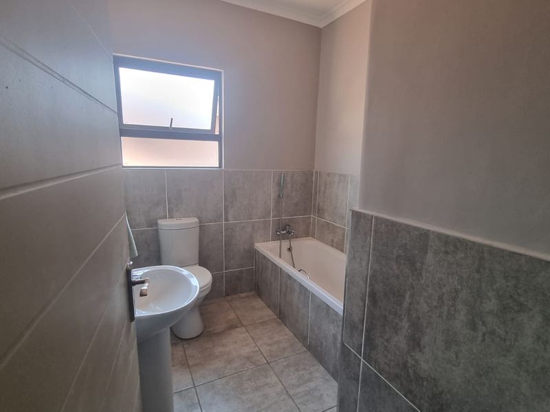 A clean, modern bathroom featuring neutral grey floor-to-ceiling wall tiles, a pedestal basin, a toilet, and a built-in bathtub.