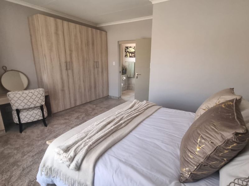 A well-maintained bedroom featuring built-in wooden cupboards, neutral carpeting, and direct access to an en-suite bathroom.